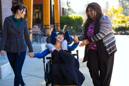Young child with disabilities in a wheelchair with two helpers